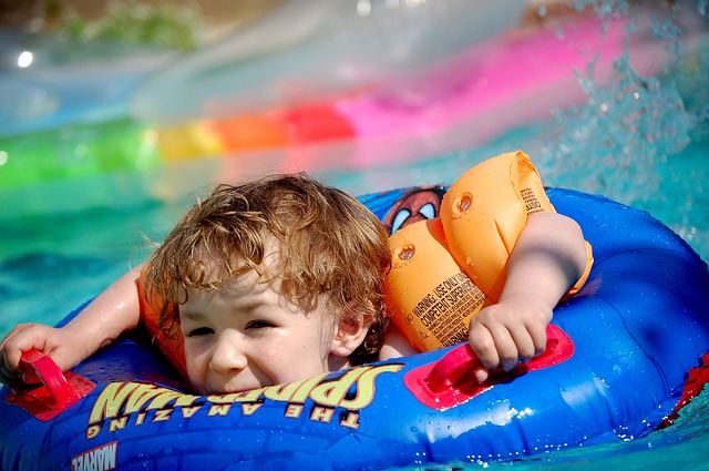 Dítě v bazénu v modrém plovacím kruhu se spidermanem a s barevnými oranžovými rukávky