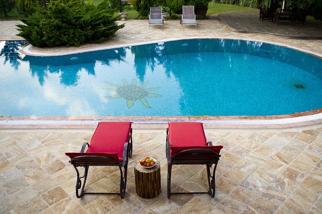 Vydlážděná terasa s bazénem, ve kterém je na zemi namalované slunce a se dvěma červenými křesly na sezení v popředí